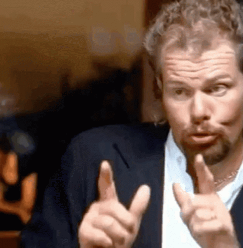 A Man With A Beard Is Making A Funny Face And Pointing At The Camera . GIF