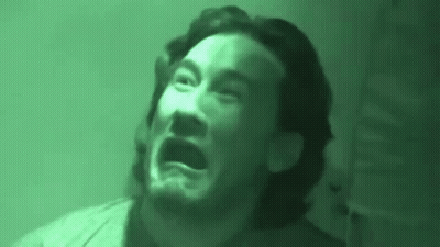 A Man With A Beard Is Making A Funny Face In A Dark Room . GIF