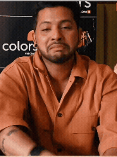 A Man With A Beard Is Making A Funny Face In Front Of A Poster That Says Colors GIF
