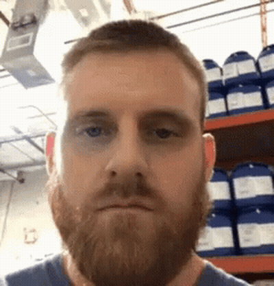 A Man With A Beard Is Making A Funny Face In Front Of A Shelf Of Chemicals . GIF