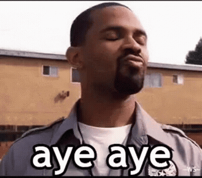 A Man With A Beard Is Making A Funny Face While Standing In Front Of A Building And Saying Aye Aye . GIF