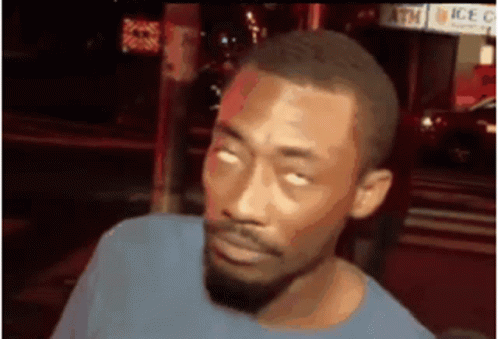 A Man With A Beard Is Making A Funny Face While Standing In Front Of A Sign That Says Atm . GIF