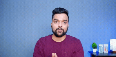A Man With A Beard Is Making A Funny Face With His Hands Outstretched In Front Of A Blue Wall . GIF