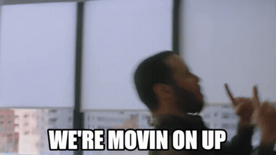 a man with a beard is making a peace sign and says `` we 're movin on up ''