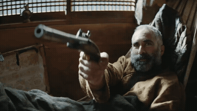 A Man With A Beard Is Pointing A Gun At The Camera GIF
