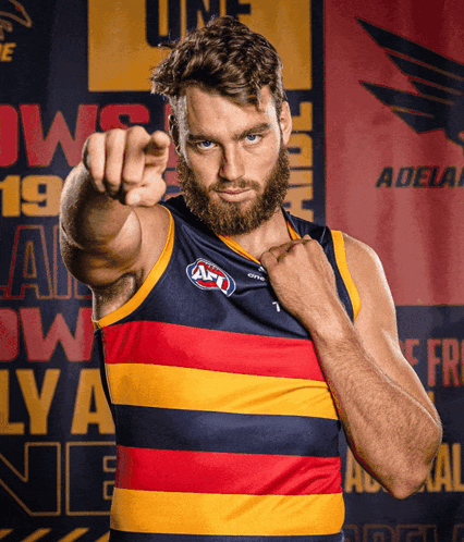 A Man With A Beard Is Pointing At The Camera In Front Of A Banner That Says Adelaide GIF