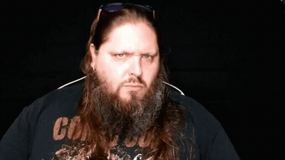 A Man With A Beard Is Pointing At The Camera While Wearing Sunglasses And A Watch . GIF
