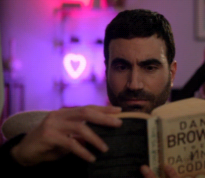 A Man With A Beard Is Reading A Book Called Dan Brown 'S Damn Code GIF