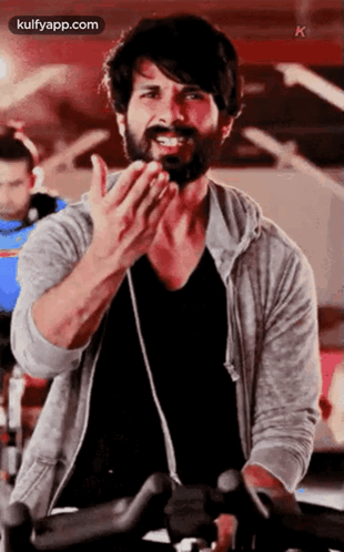 A Man With A Beard Is Riding An Exercise Bike In A Gym And Clapping . GIF