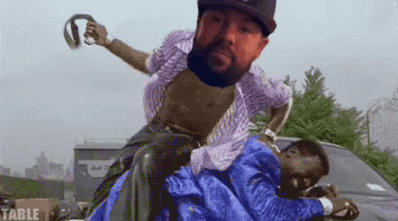 A Man With A Beard Is Riding Another Man On His Shoulders . GIF