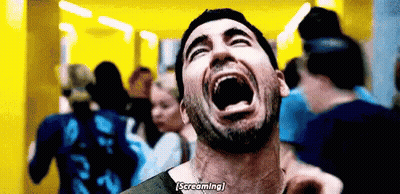 A Man With A Beard Is Screaming With His Mouth Open In Front Of A Crowd . GIF