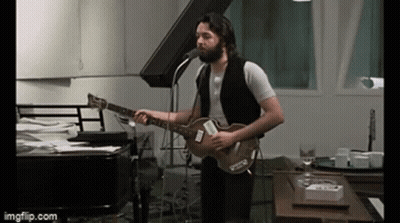 A Man With A Beard Is Singing Into A Microphone While Playing A Guitar . GIF