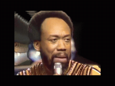 A Man With A Beard Is Singing Into A Microphone While Wearing A Striped Shirt GIF