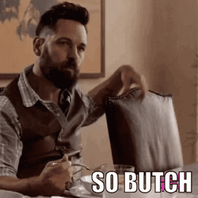A Man With A Beard Is Sitting At A Table Holding A Chair And A Cup Of Coffee . GIF