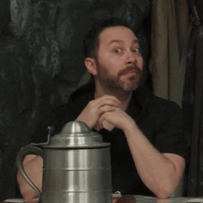 A Man With A Beard Is Sitting At A Table Next To A Metal Pitcher GIF