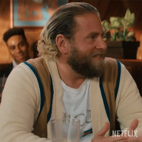 A Man With A Beard Is Sitting At A Table With A Glass Of Water And A Netflix Logo In The Corner . GIF