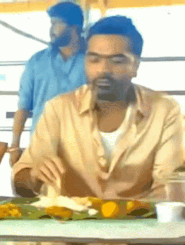 A Man With A Beard Is Sitting At A Table With A Plate Of Food In Front Of Him GIF