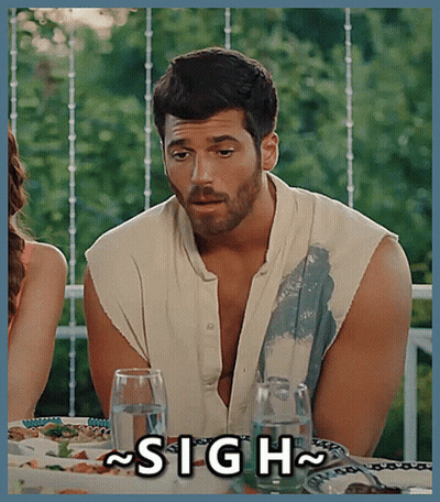 A Man With A Beard Is Sitting At A Table With A Sign That Says Sigh GIF