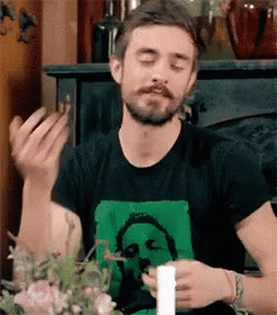 A Man With A Beard Is Sitting At A Table With His Eyes Closed And A Candle In His Hand . GIF