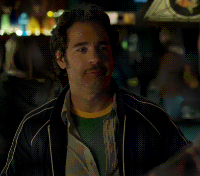 A Man With A Beard Is Sitting At A Table With His Eyes Closed In A Dark Room . GIF