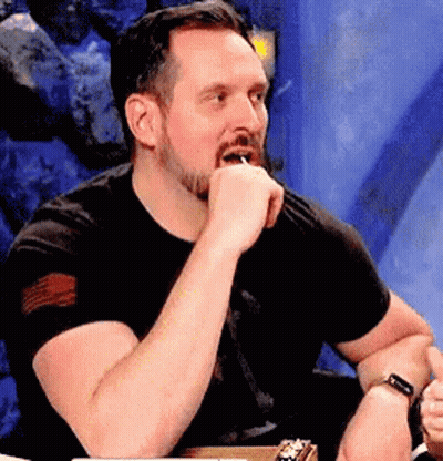 A Man With A Beard Is Sitting At A Table With His Hand On His Chin And A Watch On His Wrist . GIF