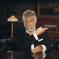 A Man With A Beard Is Sitting At A Table With His Hands Up GIF