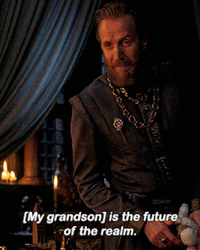A Man With A Beard Is Sitting At A Table With The Words " My Grandson Is The Future Of The Realm " Above Him GIF