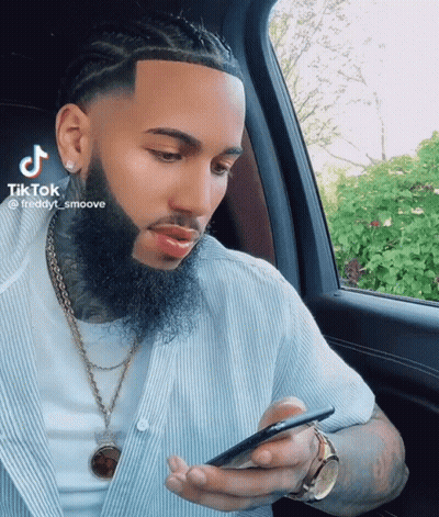 A Man With A Beard Is Sitting In A Car And Looking At His Phone GIF