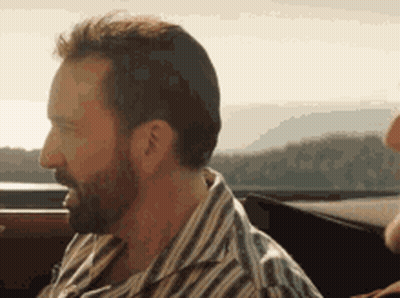 A Man With A Beard Is Sitting In A Car Looking Out The Window . GIF
