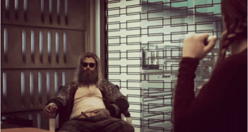 A Man With A Beard Is Sitting In A Chair And A Woman Is Taking A Picture Of Him GIF