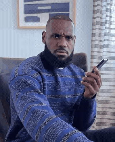 A Man With A Beard Is Sitting In A Chair And Holding A Cell Phone GIF