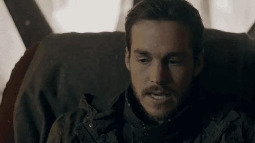 A Man With A Beard Is Sitting In A Chair And Looking At Something . GIF