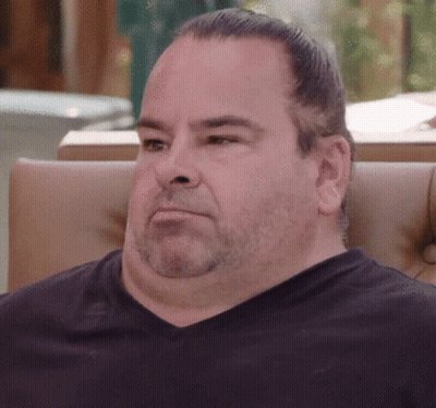 A Man With A Beard Is Sitting In A Chair And Looking At The Camera GIF