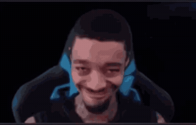 A Man With A Beard Is Sitting In A Chair And Smiling At The Camera . GIF
