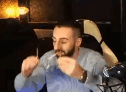 A Man With A Beard Is Sitting In A Chair Eating A Sandwich . GIF