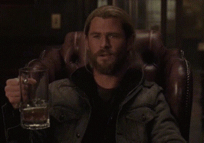 A Man With A Beard Is Sitting In A Chair Holding A Beer Mug . GIF