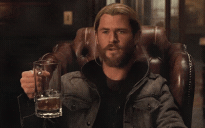 A Man With A Beard Is Sitting In A Chair Holding A Glass Of Beer GIF