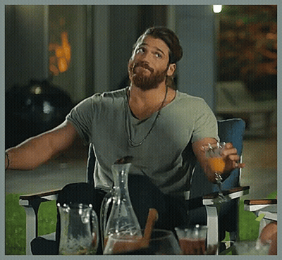 A Man With A Beard Is Sitting In A Chair Holding A Glass Of Orange Juice . GIF