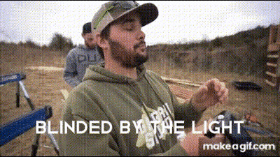 A Man With A Beard Is Sitting In A Chair In A Field With The Words Blinded By The Light Written Above Him . GIF