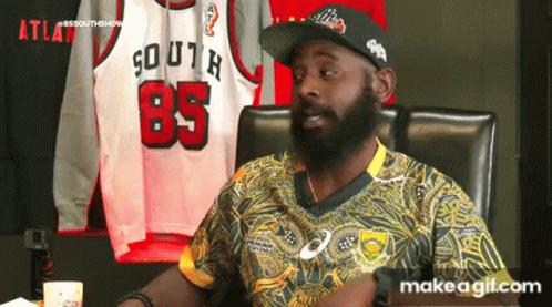 A Man With A Beard Is Sitting In A Chair In Front Of A Display Of Jerseys . GIF