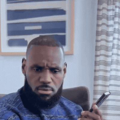 A Man With A Beard Is Sitting In A Chair Looking At A Cell Phone GIF