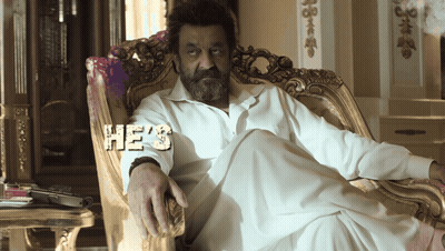 A Man With A Beard Is Sitting In A Chair With The Word He 'S On His Shirt GIF
