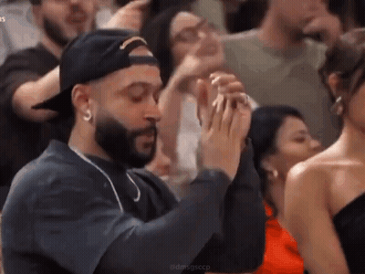 A Man With A Beard Is Sitting In A Crowd Of People Clapping Their Hands . GIF