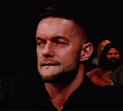 A Man With A Beard Is Sitting In A Dark Room And Looking At The Camera . GIF