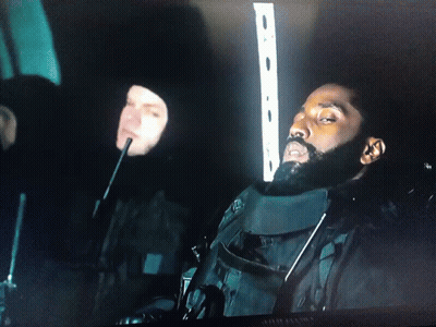 A Man With A Beard Is Sitting In A Dark Room Next To Another Man With A Microphone GIF