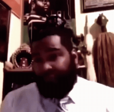 A Man With A Beard Is Sitting In A Room Looking At The Camera GIF