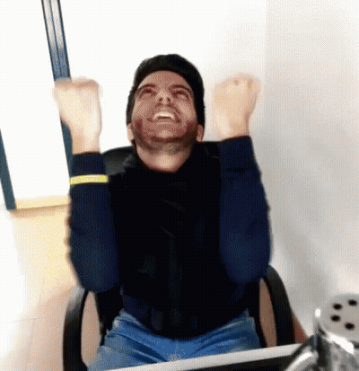 A Man With A Beard Is Sitting In An Office Chair With His Arms In The Air GIF