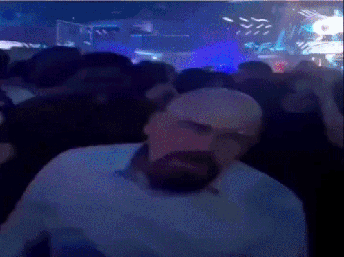 A Man With A Beard Is Sitting In Front Of A Crowd In A Club . GIF
