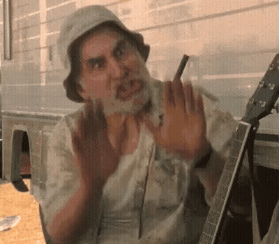 A Man With A Beard Is Sitting In Front Of A Guitar . GIF