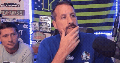 A Man With A Beard Is Sitting In Front Of A Microphone And Covering His Mouth With His Hand . GIF